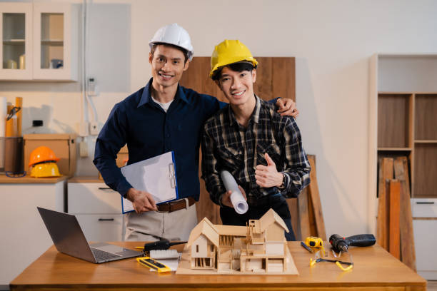 Two ADU contractors in Los Angeles wearing hard hats stand by a table displaying a model of a house, discussing construction plans