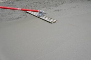 A man uses a red hose to pour concrete, illustrating the process for driveways and patios. 