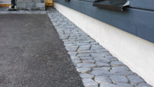 A stone walkway beside a house featuring a window, illustrating a residential outdoor space.