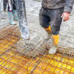 A man stands on a concrete foundation slab, highlighting the starting point of a construction project built on a strong, reliable base.