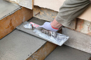 A person operates a cement mixer, pouring concrete for new front porch steps.