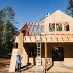 A man is in front of a newly built house with a wooden frame, emphasizing the new construction and design features.