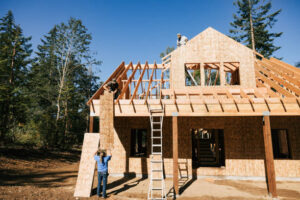 A man is in front of a newly built house with a wooden frame, emphasizing the new construction and design features.