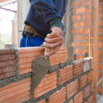 A man constructs a wall using a brick, demonstrating techniques from Wall Construction Solutions.