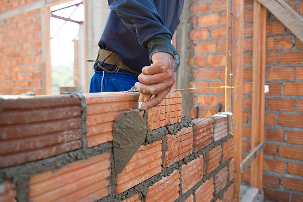 A man constructs a wall using a brick, demonstrating techniques from Wall Construction Solutions.