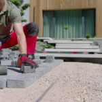 A man works on laying bricks for a patio, demonstrating careful paver installation techniques.
