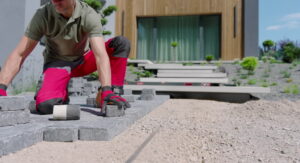 A man works on laying bricks for a patio, demonstrating careful paver installation techniques.