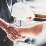 Two people shaking hands in front of a window, symbolizing partnership with a trusted general contractor in Burbank.