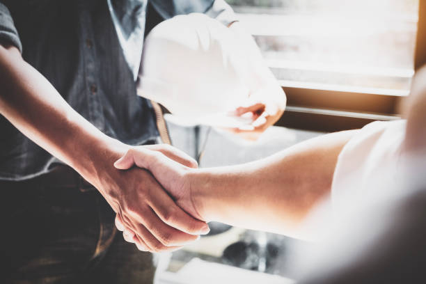Two people shaking hands in front of a window, symbolizing partnership with a trusted general contractor in Burbank.
