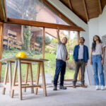 Three individuals stand in an unfinished house, discussing home remodeling ideas amidst exposed walls and construction materials.